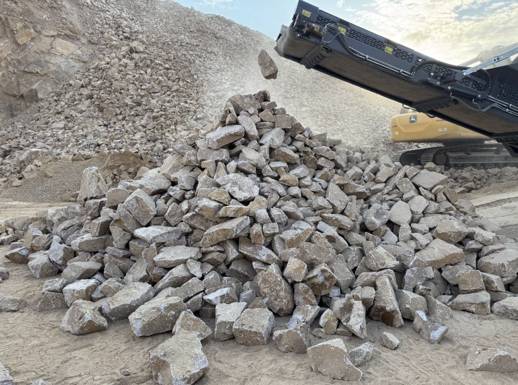 Freshly crushed riprap stockpile in front of Onyx mobile plant with Deere excavator working the quarry face